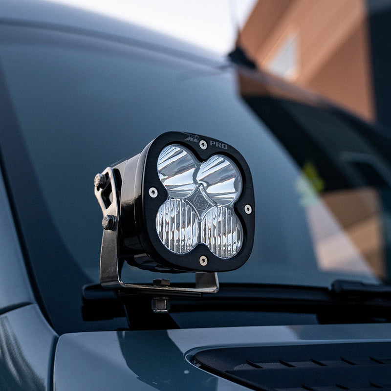 Baja Designs XL Pro A-Pillar Kit on a vehicle: A black XL Pro pod with a clear lens mounted on a bracket at the base of the windshield of a dark van