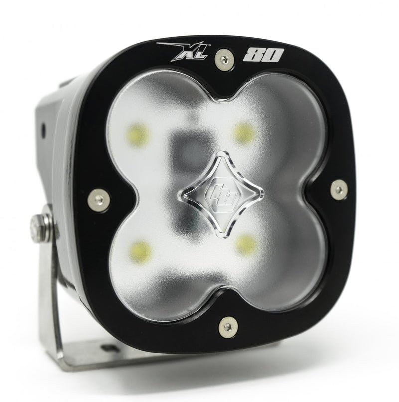 Baja Designs XL80 LED Auxiliary Light Pod, whole product on a studio background: A single black Baja Designs XL80 LED pod switched on, its clear lens glowing white, shown at an angle on white