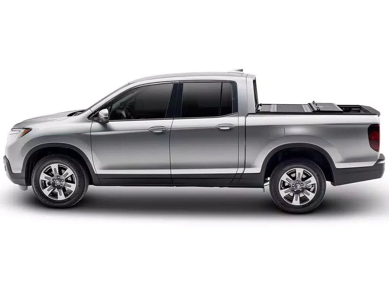 BAKFlip F1 hard folding tonneau cover folded flat and stacked at the front of the bed on a silver Honda Ridgeline, side profile on a white background