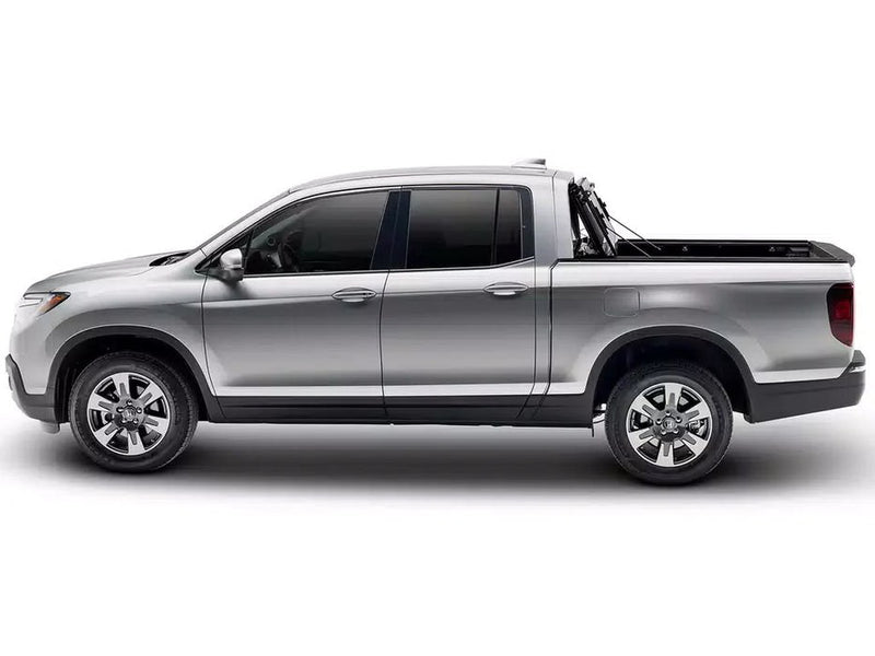 BAKFlip F1 hard folding tonneau cover folded and stacked upright against the cab of a silver Honda Ridgeline with the truck bed open, side profile on a white background