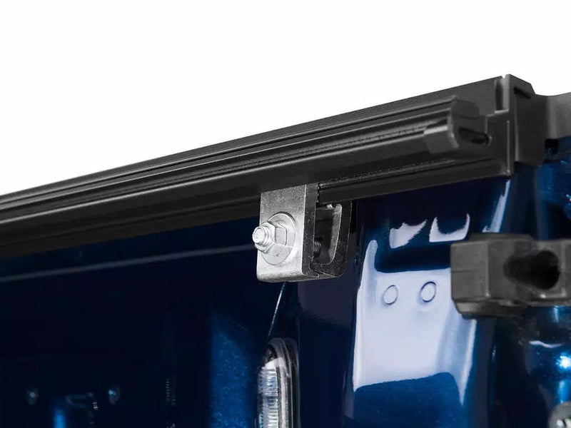 Close-up of the black side rail and polished metal clamp bolt of a BAKFlip FiberMax tonneau cover secured to the bed rail of a blue pickup truck