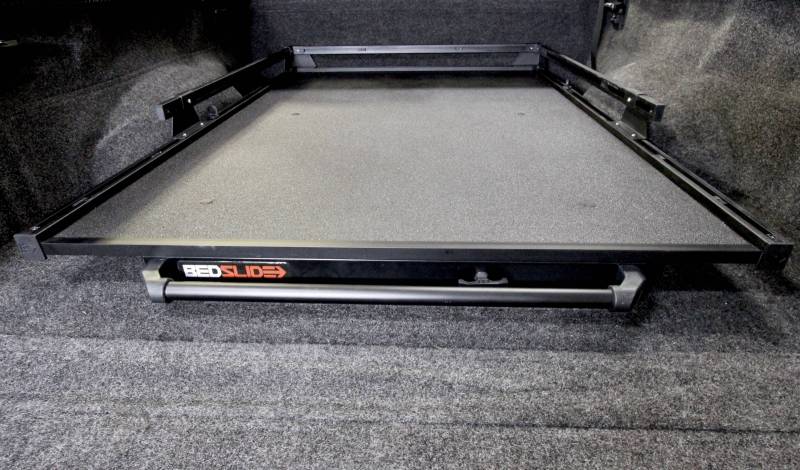 BEDSLIDE cargo slide in Black Edition finish photographed low from the tailgate showing the full width grab bar. BEDSLIDE uses this Black Edition photograph across its Classic and Heavy Duty ranges and the front rail carries no model badge, so the frame does not identify which range it shows.
