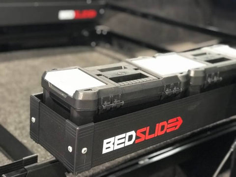 Black Edition BEDSLIDE BEDBIN Side Kix bin loaded with stacked tool cases, showing the white and red BEDSLIDE decal on the matte black extrusion