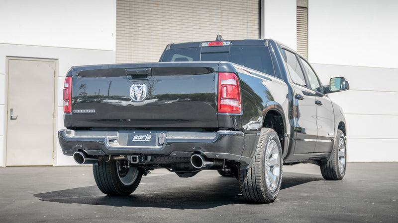 Borla ATAK Cat-Back Exhaust System installed on a Ram 1500: A black Ram 1500 crew cab seen from the rear quarter with dual rear exhaust tips and a Borla plate on the bumper