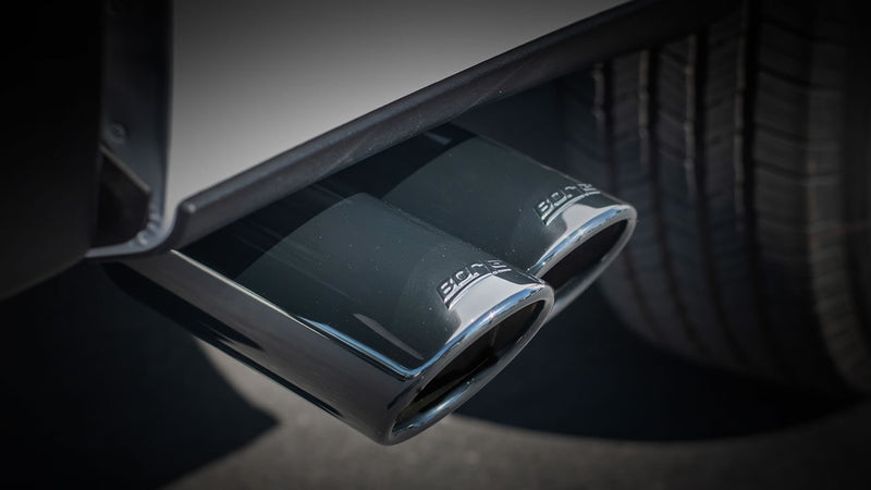 Borla ATAK Cat-Back Exhaust System on a vehicle: A close-up of twin black chrome Borla exhaust tips exiting beneath a vehicle's rear bumper