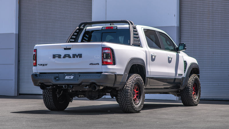 Borla ATAK Mid-Section Exhaust System installed on a Ram 1500 TRX: white Ram 1500 TRX with a roll bar, rear three-quarter view in front of garage doors, exhaust tips under the rear bumper