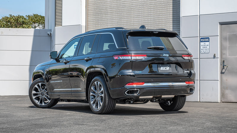 Borla S-Type Cat-Back Exhaust System installed on a Jeep Grand Cherokee: A black Jeep Grand Cherokee parked beside a white building, seen from the rear three-quarter