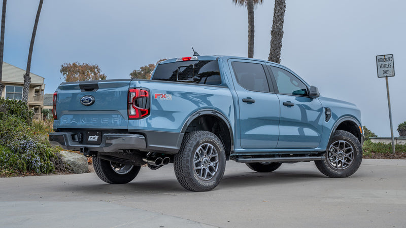Borla S-Type Cat-Back Exhaust System installed on a Ford Ranger: light blue Ford Ranger FX4 parked by palm trees with dual exhaust tips ahead of the rear wheel and a Borla plate