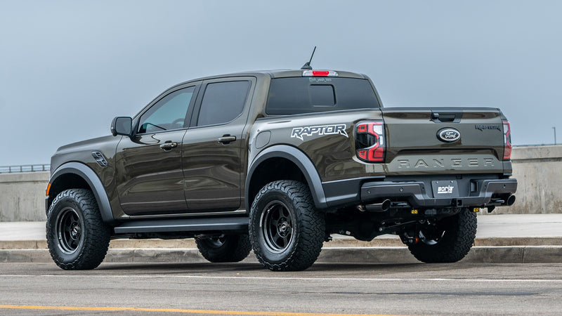 Borla Tail Pipe Kit installed on a Ford Ranger Raptor: A green-gray Ford Ranger Raptor is parked by a seawall with Raptor decals on the bedside