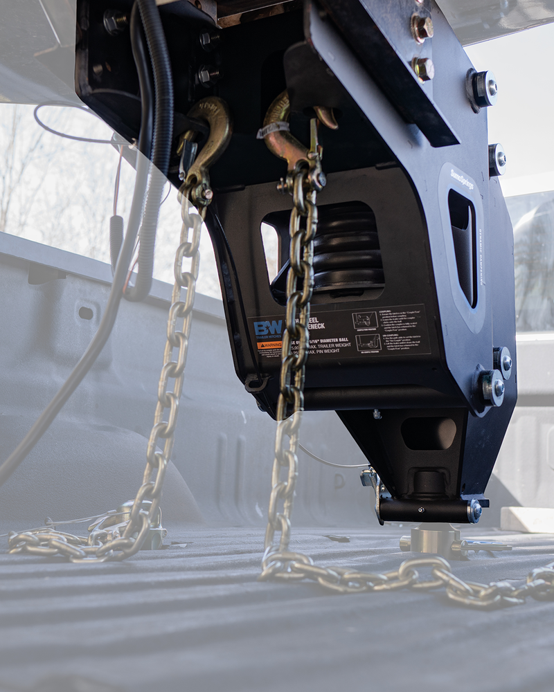 Underside view of a B&W fifth wheel to gooseneck adapter on a trailer pin box with safety chains attached