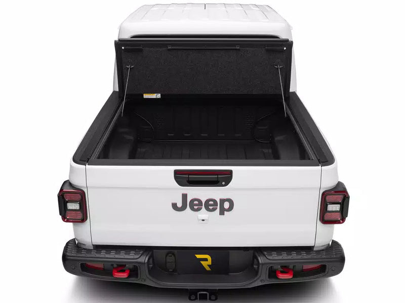 UnderCover Ultra Flex hard folding tonneau cover folded fully open and standing upright against the bulkhead, straight rear view along the empty bed floor.