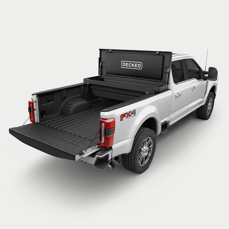 Black DECKED Tool Box mounted crossbed behind the cab of a white Ford Super Duty, lid open, showing the mounting position and remaining bed space