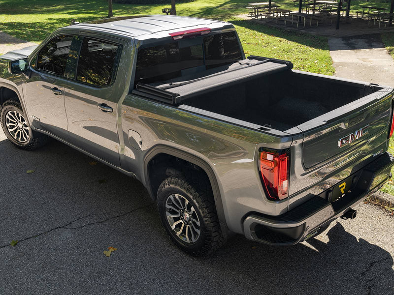 Soft tonneau cover partly folded on a gray pickup parked outdoors