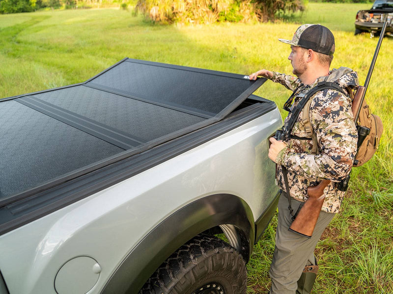 Gator EFX hard folding tonneau cover: A hunter lifts the rear panel of a black hard folding cover on a silver off-road pickup in a grassy field