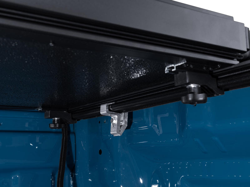 Close-up of the Gator EFX tonneau cover: close-up from inside a blue truck bed of the folded cover stack, its rail clamp and prop hardware