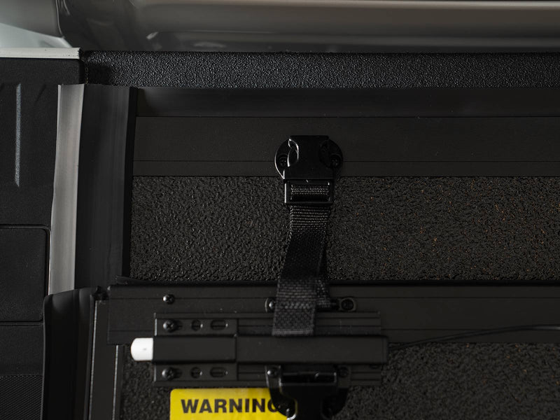 Gator EFX hard folding tonneau cover: Close-up of the strap and latch hardware on the underside of a cover panel with a yellow warning label