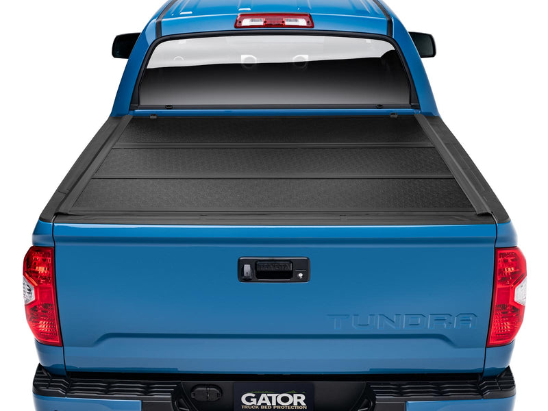 Gator EFX hard folding tonneau cover: Rear view of a blue Toyota Tundra with a closed black hard folding tonneau cover and a Gator hitch plate