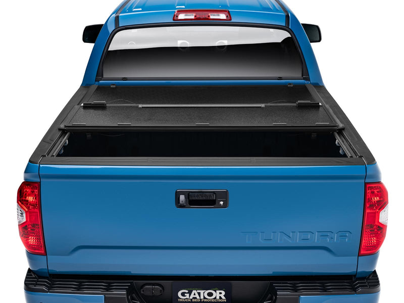 Gator EFX tonneau cover (partial) on a Toyota pickup: rear view of a blue Toyota with the rear panel of a black hard folding tonneau cover folded forward