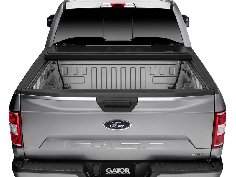 Gator EFX hard folding tonneau cover: Rear view of a silver Ford F-150 with the hard tri-fold cover folded up at the cab and the bed open