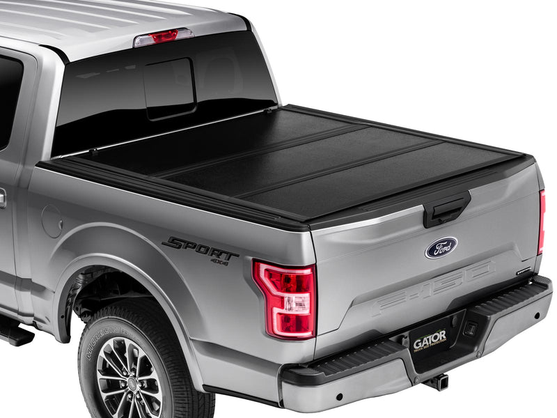 Gator EFX hard folding tonneau cover: Silver full-size pickup from the rear three-quarter with a closed black hard tri-fold tonneau cover