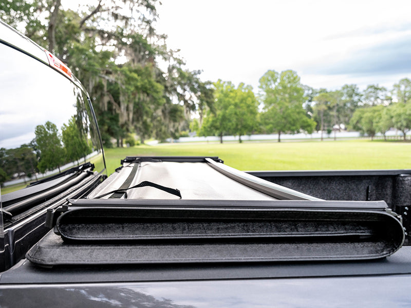 Gator SFX tonneau cover (open) on a pickup bed: folded soft cover stack at the front of a truck bed with a park and trees in the background