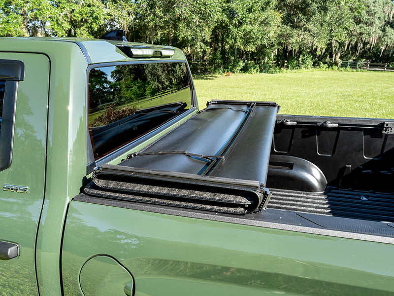 Gator SFX tonneau cover (open) on a pickup bed: the folded soft cover stack at the front of a green truck bed, trees in the background