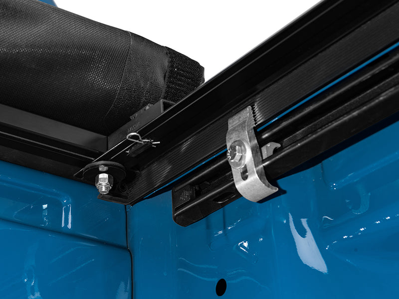 Gator SRX soft roll-up tonneau cover: Close-up of a soft roll-up tonneau side rail and its metal clamp mounted under a blue truck bed rail