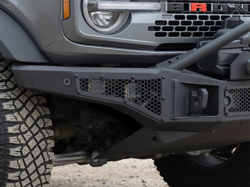 Go Rhino Rockline: close-up of a textured black bumper wing with hex mesh and shackle mount below a round headlamp (shown with cube lights, not included)
