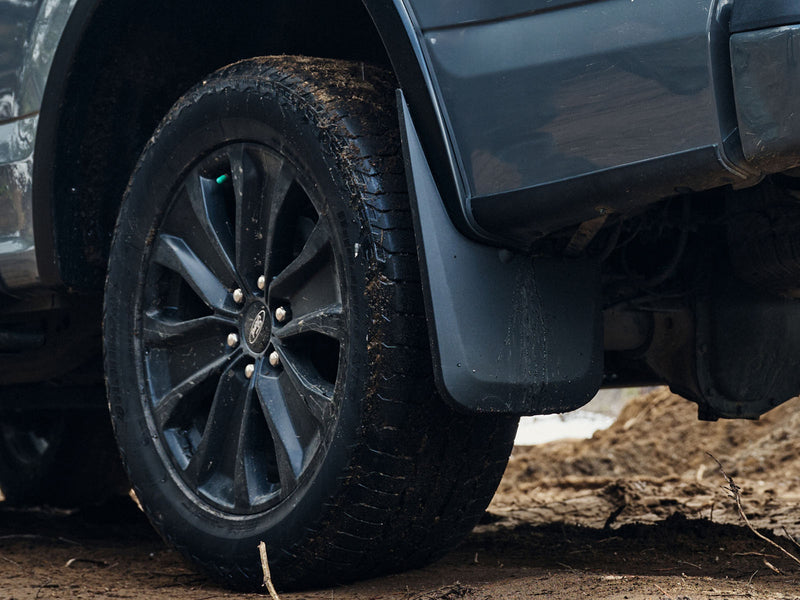 Husky Liners Custom Molded: black mud guard installed behind the wheel of a gray Ford truck on a muddy trail