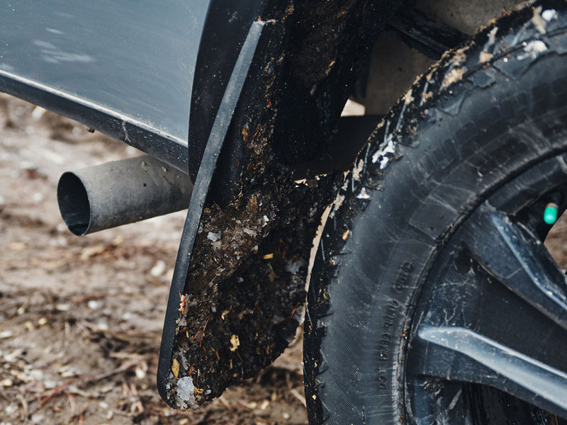Husky Liners Custom Molded: close-up of a mud-covered black mud guard behind a tire, exhaust pipe in background