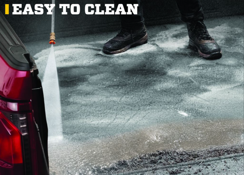 Husky Liners Guardian Comfort: pressure-washer spray cleaning a gray carpet bed mat in a red pickup bed while a person in boots stands on it