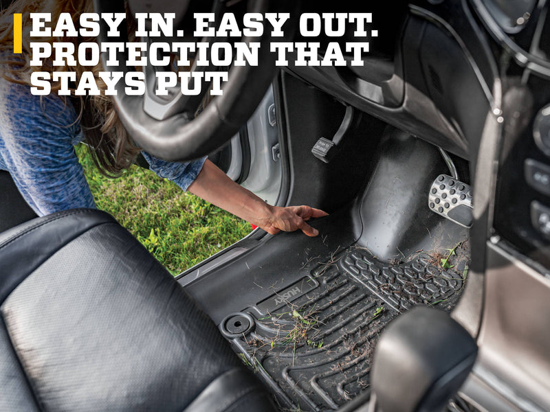 Husky Liners WeatherBeater: hand lifting a black driver-side floor liner with grass debris from a footwell