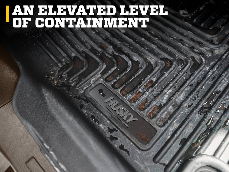Husky Liners X-act Contour: close-up of a dirty black floor liner showing ribs and the Husky logo plate