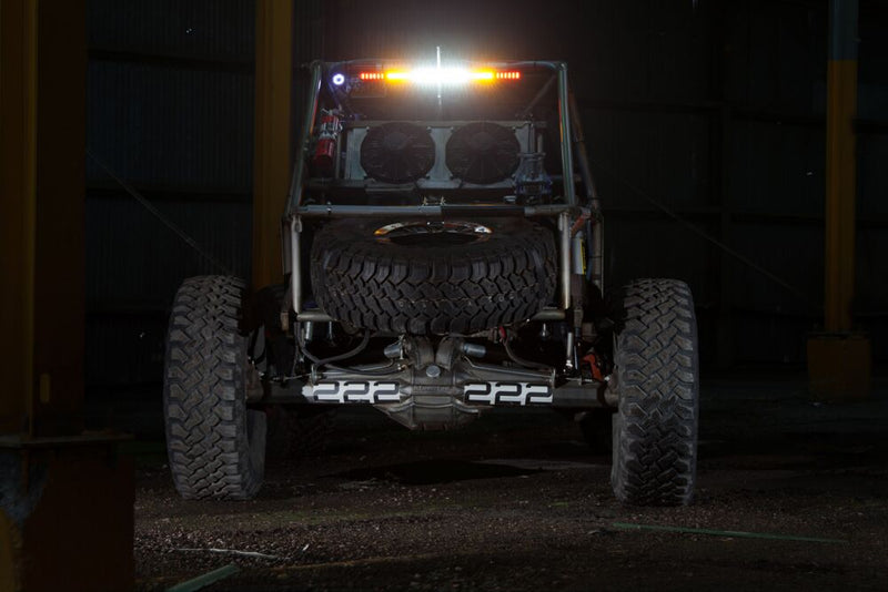 KC HiLiTES 28" Multi-Function Rear-Facing Chase LED Light Bar on a vehicle: rear view of a rock crawler buggy at night with a lit amber and white chase light bar across the top of the roll cage