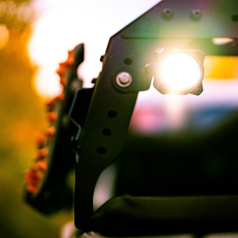 KC HiLiTES FLEX ERA 1 LED Light Pod Master Kit on a vehicle: A lit FLEX ERA 1 LED light pod mounted on a black steel bracket at sunset