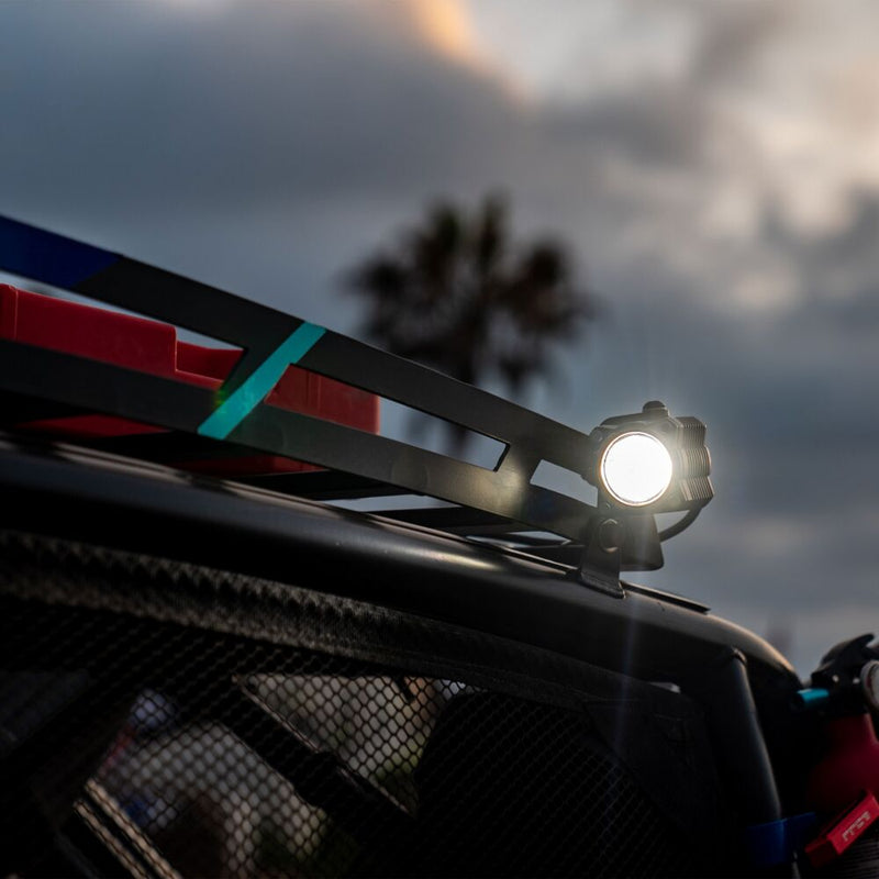KC HiLiTES FLEX ERA 1 LED Light Pod Master Kit on a vehicle: A lit FLEX ERA 1 LED pod mounted on the roof rack of a side-by-side under a cloudy sky