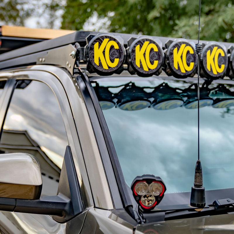 KC HiLiTES Universal Wire Hider with KClips installed on a Toyota: wire hider strip installed along the windshield pillar of a gray truck, below a row of KC lights on the roof rack and beside a ditch light