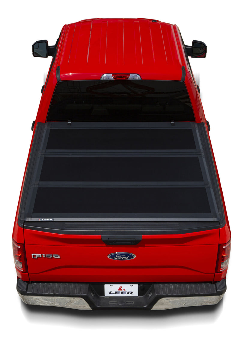 LEER HF350M hard folding tonneau cover on a pickup bed: overhead rear view of a black hard tri-fold cover closed over a red pickup bed