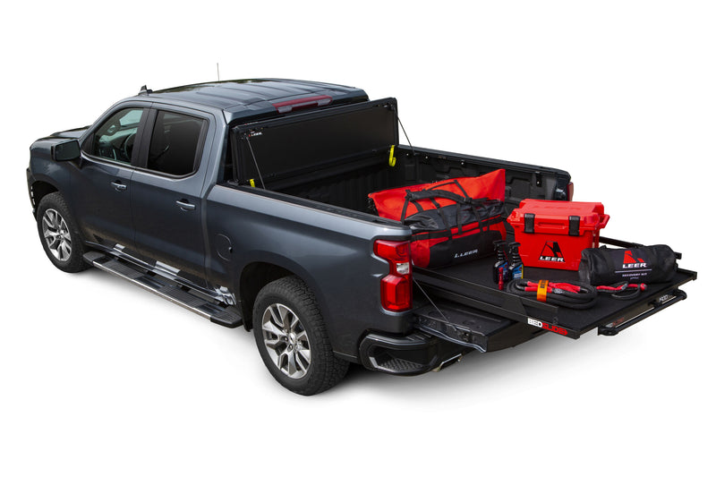 LEER HF650M hard folding tonneau cover on a pickup bed: hard folding cover stood against the cab while an extended sliding cargo tray holds bags and a cooler (bed slide, cargo in bed and cooler shown, not included)