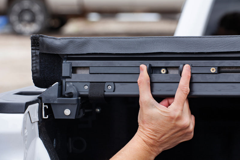 Close-up of the LEER SR250 soft roll-up tonneau cover: hand pulling the rear rail of a black vinyl roll-up cover over the tailgate end of a bed