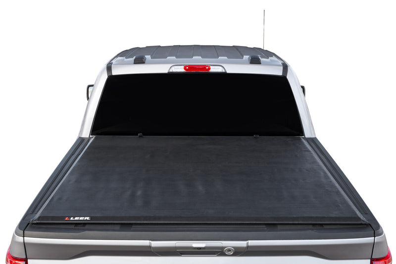 LEER SR250 soft roll-up tonneau cover on a pickup bed: rear view of a silver pickup bed with a black soft roll-up cover closed flat; cab, rear window and tailgate top in frame