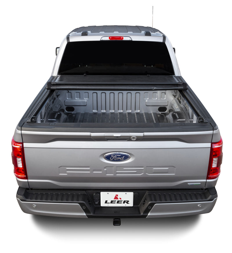 LEER SR250 soft roll-up tonneau cover on a pickup bed: rear view of a silver pickup with the black roll-up cover rolled back to the cab, open bed visible