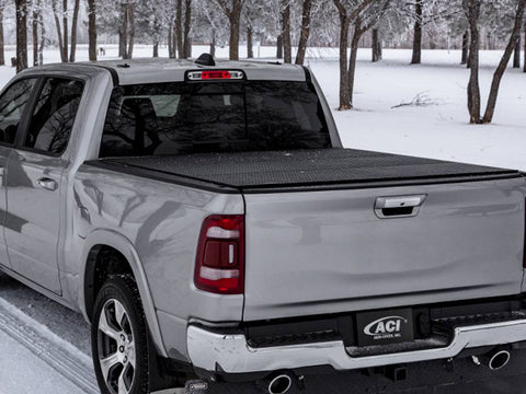 Silver pickup in a snowy wood, diamond-pattern black hard tonneau cover closed over the bed