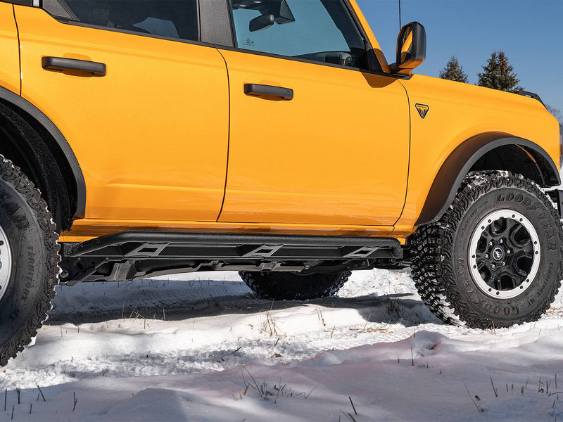 N-Fab TrailSlider step system in textured black, side profile, installed along the rocker in snow, on a Ford Bronco