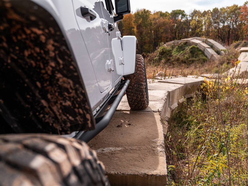 N-Fab TrailSlider step system in textured black, low view, installed along the rocker on a forest trail, on a Jeep Gladiator JT