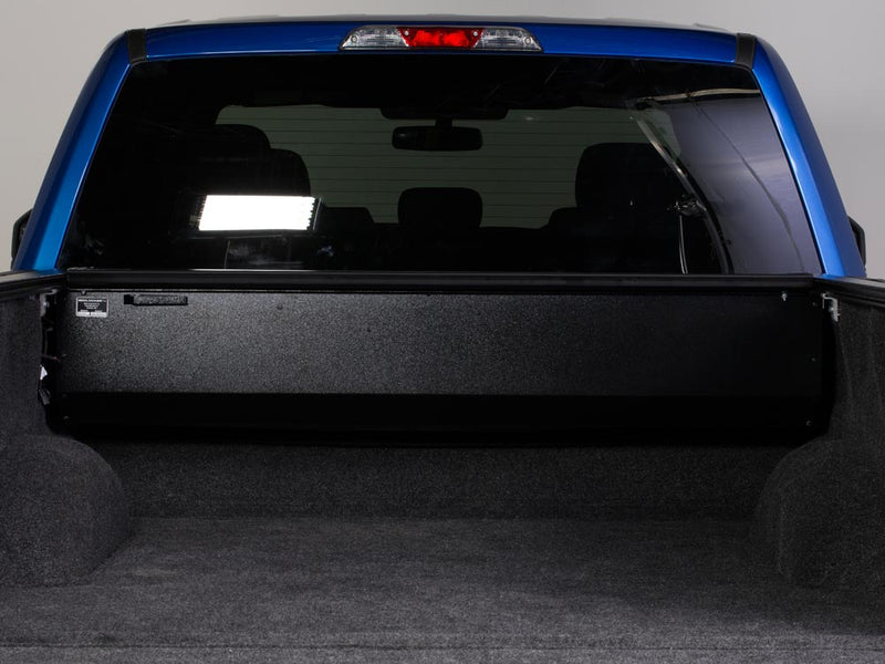 Pace Edwards BedLocker: black canister at the front of a carpeted truck bed with the cover fully retracted