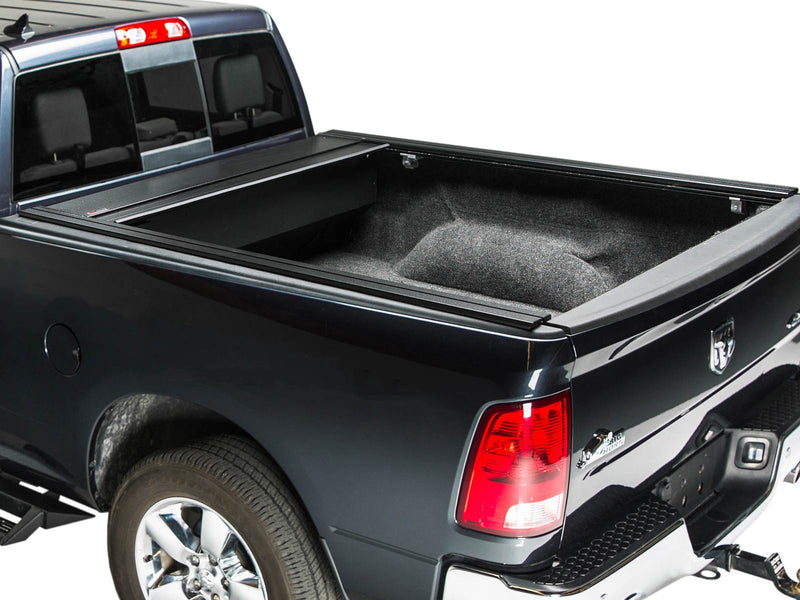 Pace Edwards BedLocker: black pickup with the retractable cover fully retracted into the canister, exposing a carpeted bed