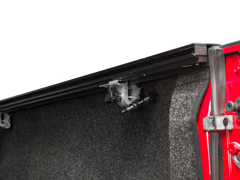 Pace Edwards BedLocker: rail mounting clamp under the side rail at the tailgate end of a carpet-lined red truck bed