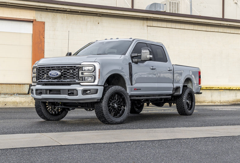 ReadyLIFT Coil Spring Front Lift Kit installed on a Ford F-250 Super Duty: gray Ford Super Duty crew cab on black wheels in front of a cream warehouse