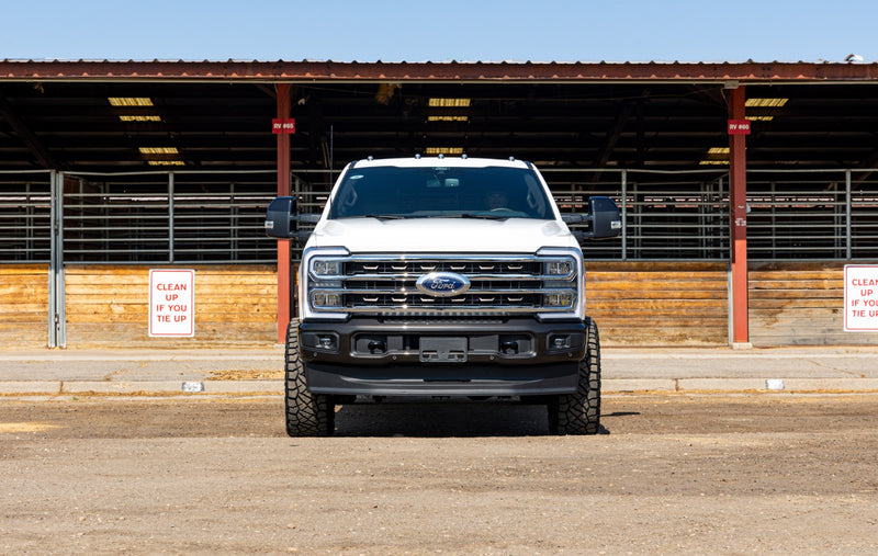 ReadyLIFT Coilover Front Lift Kit installed on a Ford F-250 Super Duty: white Ford Super Duty head-on in front of livestock pens